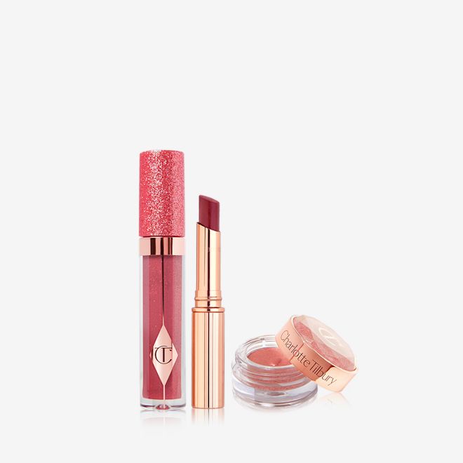 Jewel Eye Lip Secrets in Walk of No Shame open Glittery lip gloss in a berry pink shade in a glass tube with a glittery lid, sheer lipstick in a berry pink shade, and russet rose cream eyeshadow in a glass pot with its lid next to it.