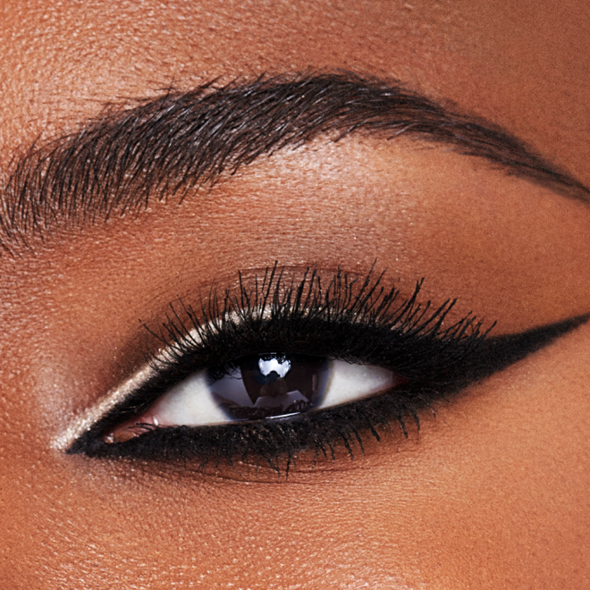 Single eye close-up of a deep-tone model with brown eyes wearing a duo eyeliner in black and champagne-beige on her upper lid and lower waterline. 