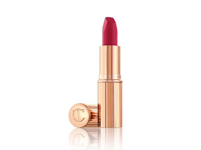 An open, matte, fuchsia-coloured lipstick in rose gold packaging with the lid next to the tube.