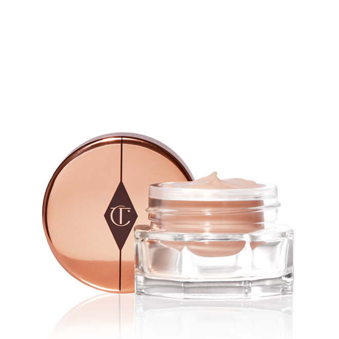 An open, light champagne-coloured eye cream in a glass pot with its rose-gold-coloured lid next to it. 