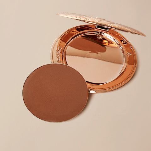An empty bronzer compact with a mirrored lid with a dark brown-coloured bronzer refill placed next to it.