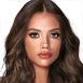 A medium-tone model with brown eyes wearing smokey brown eye makeup with warm bronze and pink blush, and glossy terracotta lips.