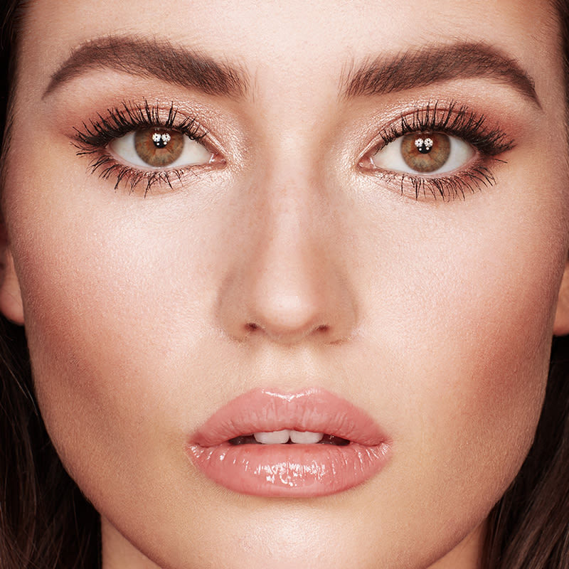 Close-up of a light-tone model with hazel eyes wearing shimmering, rose-gold eyeshadow with nude-pink lip gloss. 