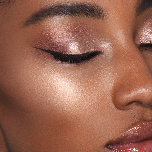 Close-up of a deep-tone model wearing shimmery rose-gold eyeshadow and black eyeliner with a glowy yet subtle, pearlescent highlighter in a rose-gold shade.