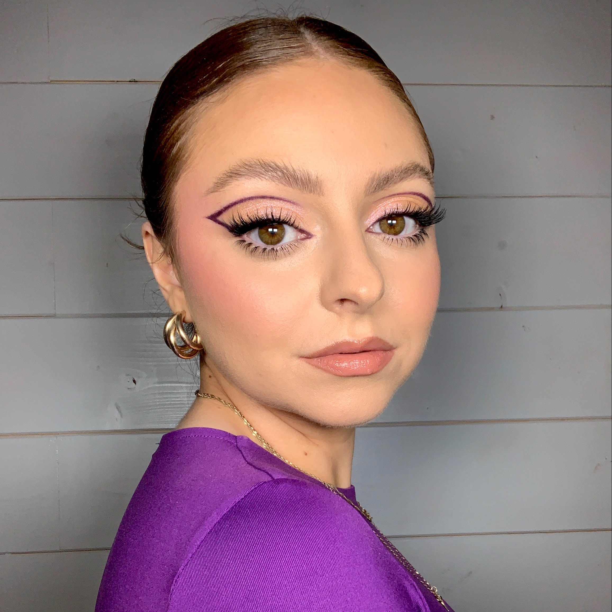 Light-tone model with brown eyes wearing soft pinkish-beige eyeshadow with black eyeliner and glitter purple eyeliner bordering her eyelid for a dramatic purple eye look.
