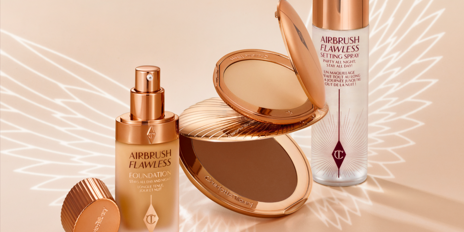 Banner with a collection of makeup that includes a setting spray, setting powder compact, foundation in a frosted glass bottle with a pump dispenser, and a bronzer compact, all in sleek, gold-coloured packaging