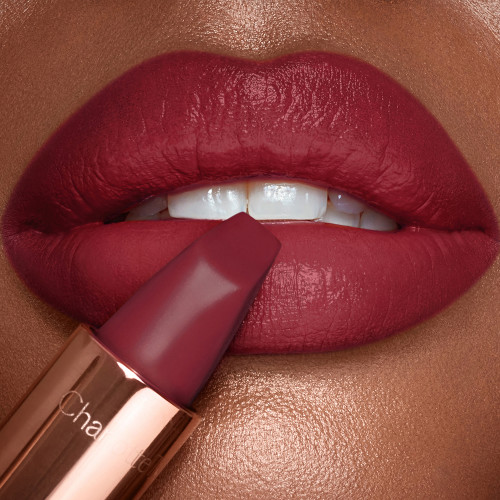 Lips close-up of a deep-tone model wearing a matte lipstick in a soft, muted berry-rose colour. 