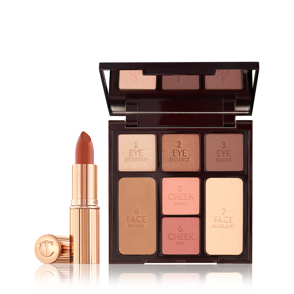 An open, mirrored-lid face palette with nude eyeshadows, nude pink and berry-pink blushes, light brown bronzer, and champagne highlighter with an open lipstick in a dark terracotta colour in a gold-coloured tube.