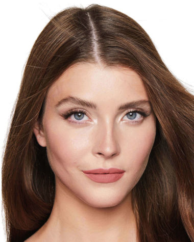 A fair-tone model with blue eyes wearing shimmery fawn and cream eyeshadow with a warm, peachy-nude matte lipstick.