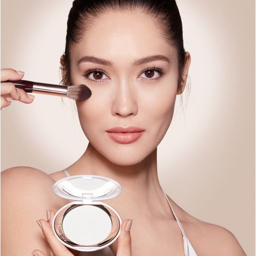 Model holding Charlotte's Airbrush Brightening Powder and applying product to the face with a brush
