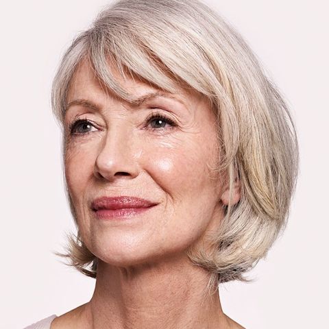 A fair-tone model with mature skin wearing natural, glowy makeup with a muted red lip shade. 
