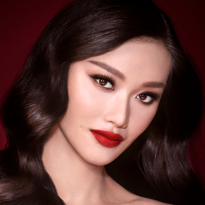 A fair-tone model with brown eyes wearing shimmery bronze eye makeup with muted pink blush and glossy scarlet-red lips