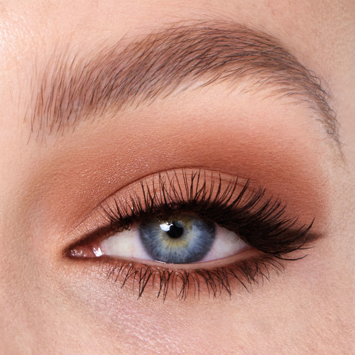 Single-eye close-up of a fair-tone model with blue eyes wearing a smokey dark brown, light brown, and gold eye look with black wing eyeliner.