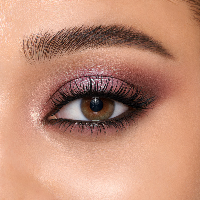 Single-eye close-up of a light-tone model with hazel eyes wearing chrome and matte eyeshadow in shades of plum, teal, and burgundy with black eyeliner. 