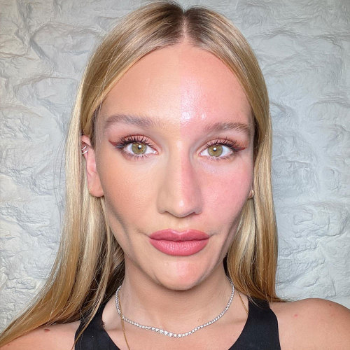 Sofia Tilbury with half face bare and the other half with skin looking smooth and flawless, and rose-gold eye makeup, black eyeliner, and bright pink lipstick on. 
