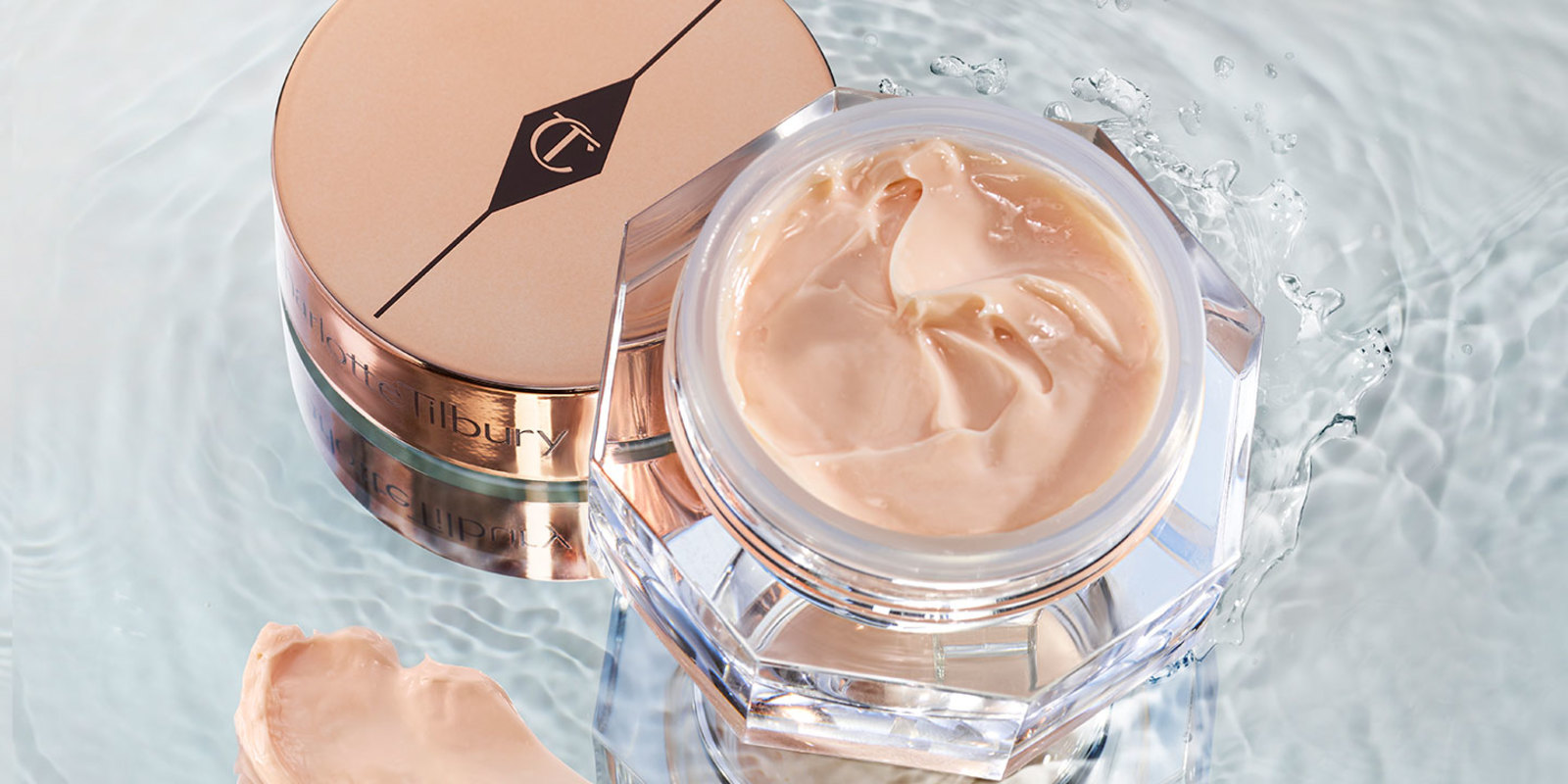 An open, petite jar filled with a thick peach-coloured eye cream with its golden-coloured lid next to it, both on top of crystal-clear water.