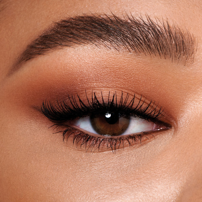 Single-eye close-up of a medium-tone model with brown eyes wearing smokey brown eye makeup with black smoked-out eyeliner.