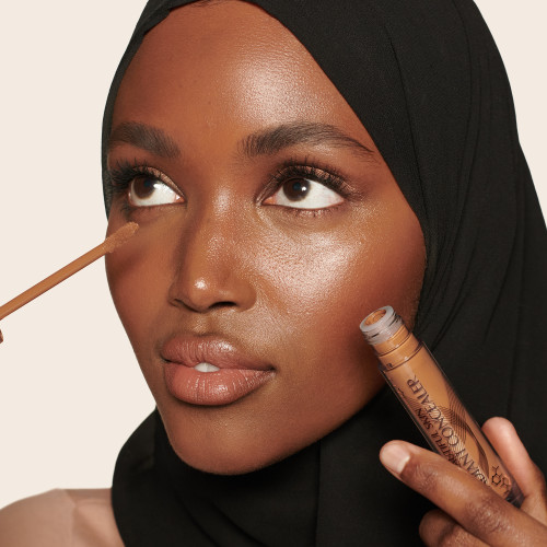 A deep-tone model applying a radiant, skin-like concealer on the other side that covers her freckles, wrinkles, and dark circles.
