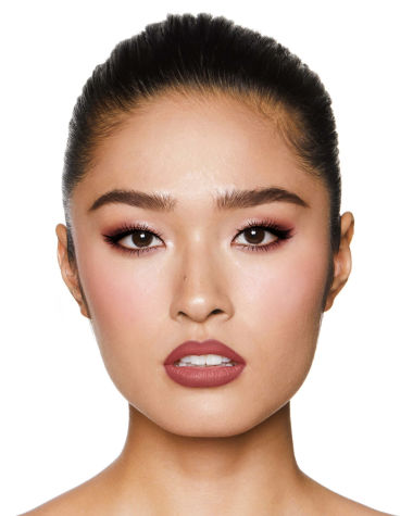 A fair-tone model with brown eyes wearing shimmery brown and gold eyeshadow with black kohl liner on her upper lid and lower waterline, a cool-toned glowy pink blush, and a berry-pink matte lipstick. 