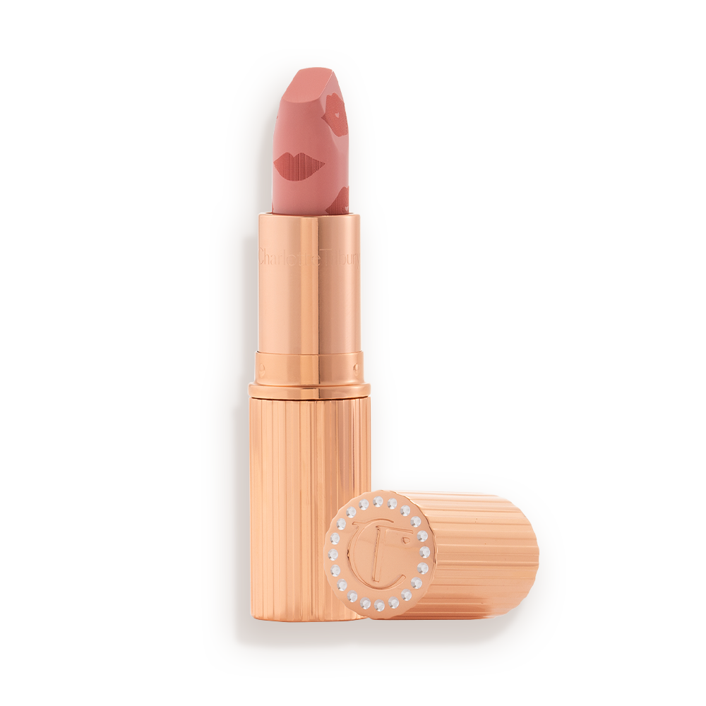 An open lipstick in a muted pink shade in a gold-coloured tube with its lid next to it.