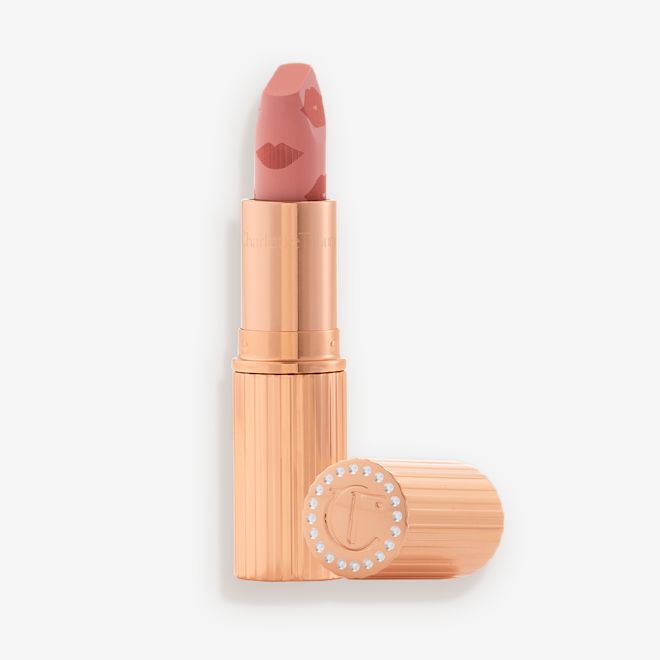 K.I.S.S.I.N.G in Famously Pink open An open lipstick in a muted pink shade in a gold-coloured tube with its lid next to it.