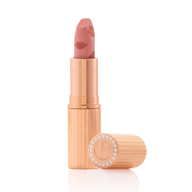 An open lipstick in a muted pink shade in a gold-coloured tube with its lid next to it.