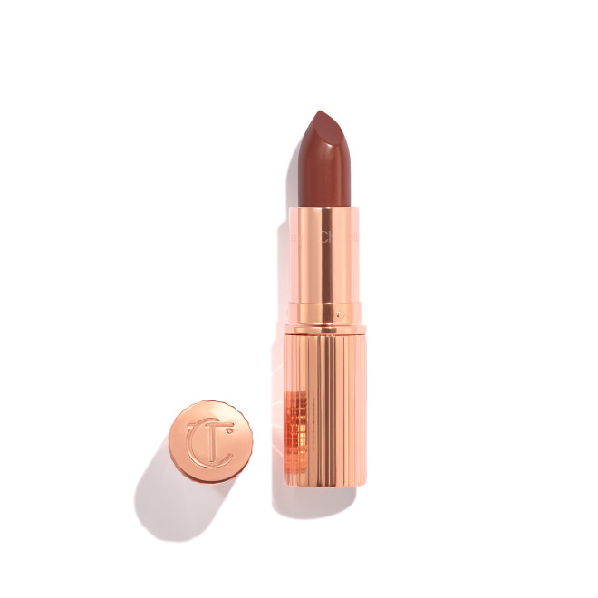 Opened, berry-pink lipstick in a metallic, golden case with its lid that's embossed with CT placed next to it. 