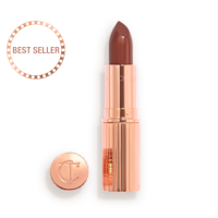 Opened, berry-pink lipstick in a metallic, golden case with its lid that's embossed with CT placed next to it. 