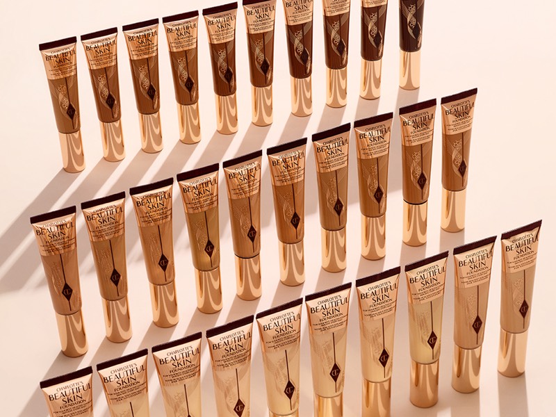 Banner with a collection of foundation tubes with the packaging the colour of the product inside on a light beige background.