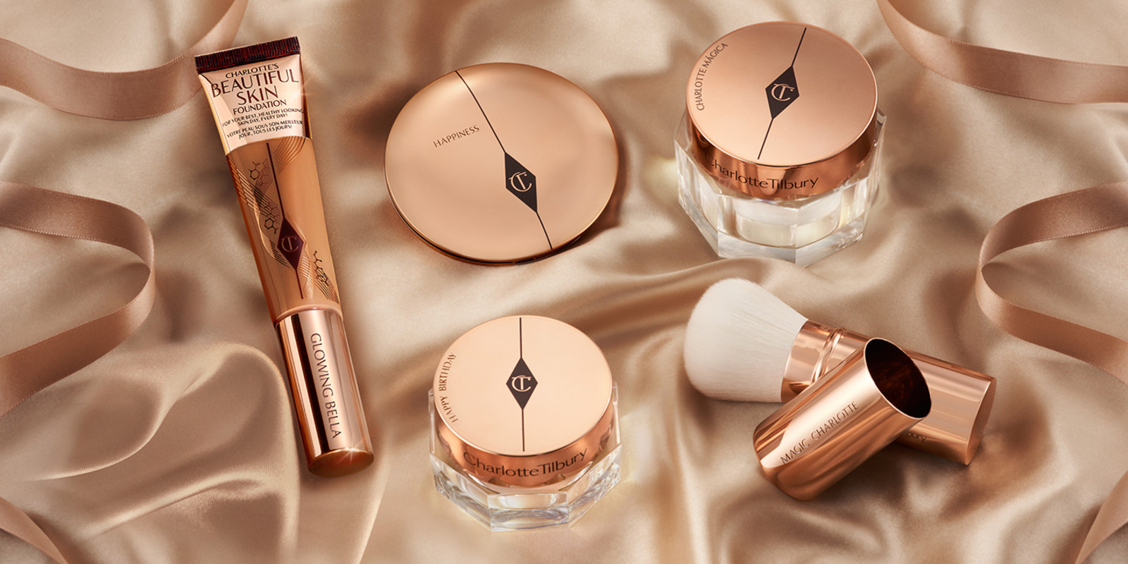 Banner with a foundation in a tube, engraved bronzer compact, engraved face cream with a gold-coloured lid, eye cream with an engraved, gold-coloured lid, and an engraved bronzer brush.