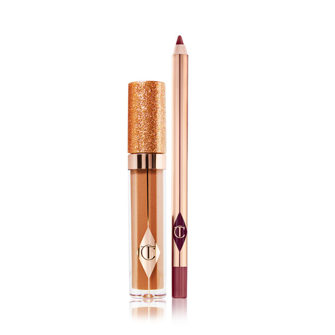 A shimmery Lip gloss in a bronze-gold shade in a glass tube with a glittery lid with a lip liner pencil in a dark winter berry shade.
