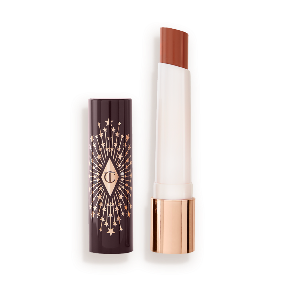 An open lipstick lip balm in a sheer peachy-nude shade, in white and gold tube with a black-coloured lid with gold sparkles all over it.