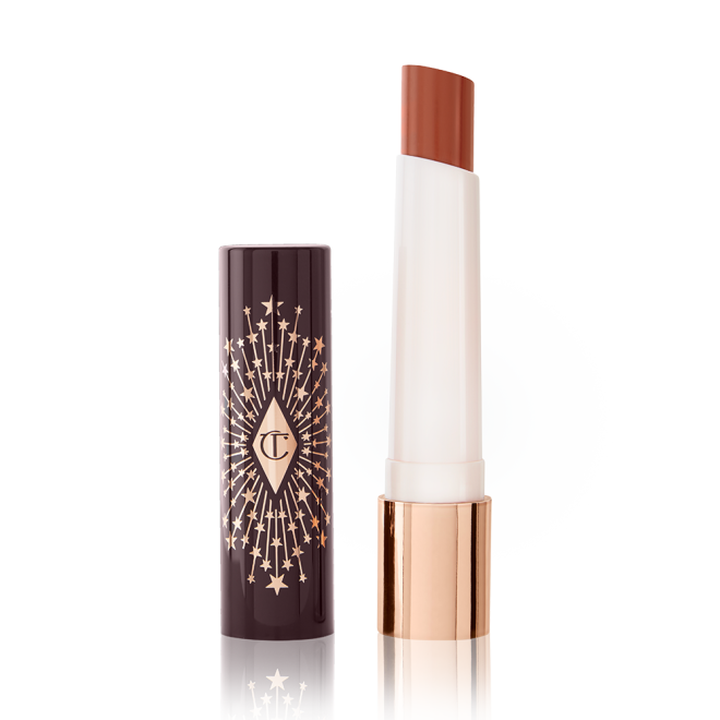 An open lipstick lip balm in a sheer peachy-nude shade, in white and gold tube with a black-coloured lid with gold sparkles all over it.