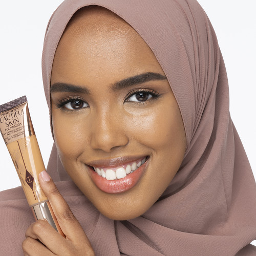 Dark-tone hijabi model wearing glowy, skin-like foundation with a satin finish with nude lipstick and subtle eye makeup.