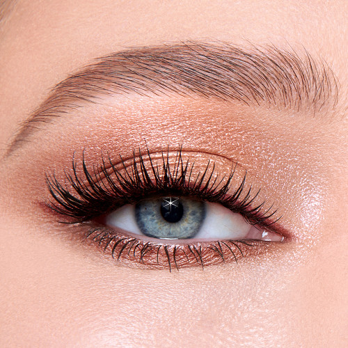 Single-eye close-up of a fair-tone model with blue eyes wearing shimmery fawn, gold, and brown eyeshadow with brown eyeliner and lengthening mascara. 