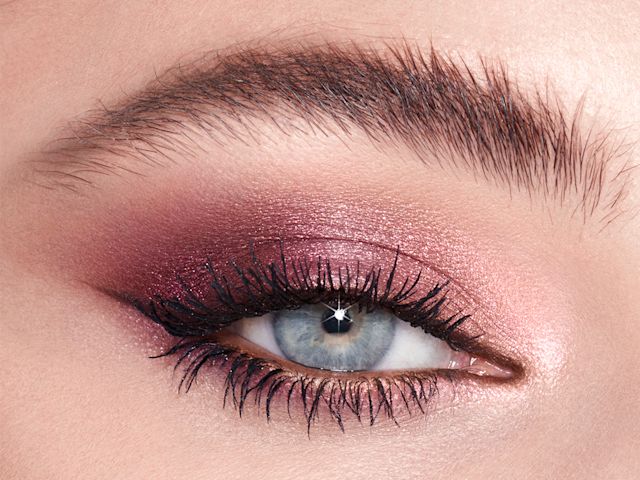 Single-eye close-up of a fair-tone model with blue eyes wearing shimmery rose gold and purple eyeshadow. 