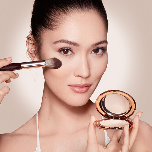A fair-tone model wearing glowy makeup and applying a radiant, setting powder that brightens, cover blemishes, and makes her skin look fresh. 