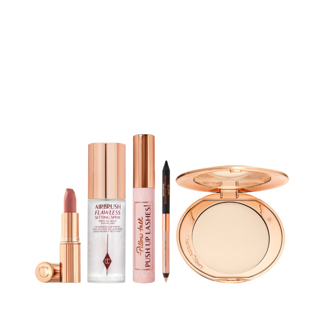 Open lipstick tube in nude pink, setting spray in a clear bottle with a gold-coloured lid, black mascara in a nude pink tube with a gold-coloured lid, double-sided eyeliner in nude beige and black, and an open setting powder compact with a mirrored-lid.
