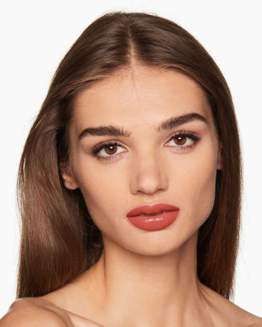 Medium-tone model with brown eyes wearing a moisturising lipstick balm in a soft glossy coral shade with a high-shine finish.