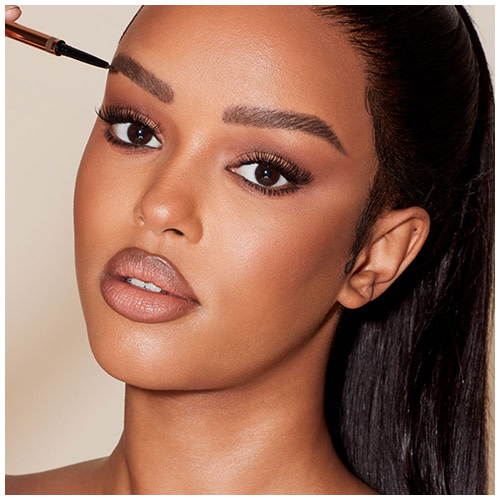 Deep-tone model with brown eyes filling in her brows with a dark brown-coloured eyebrow pencil.