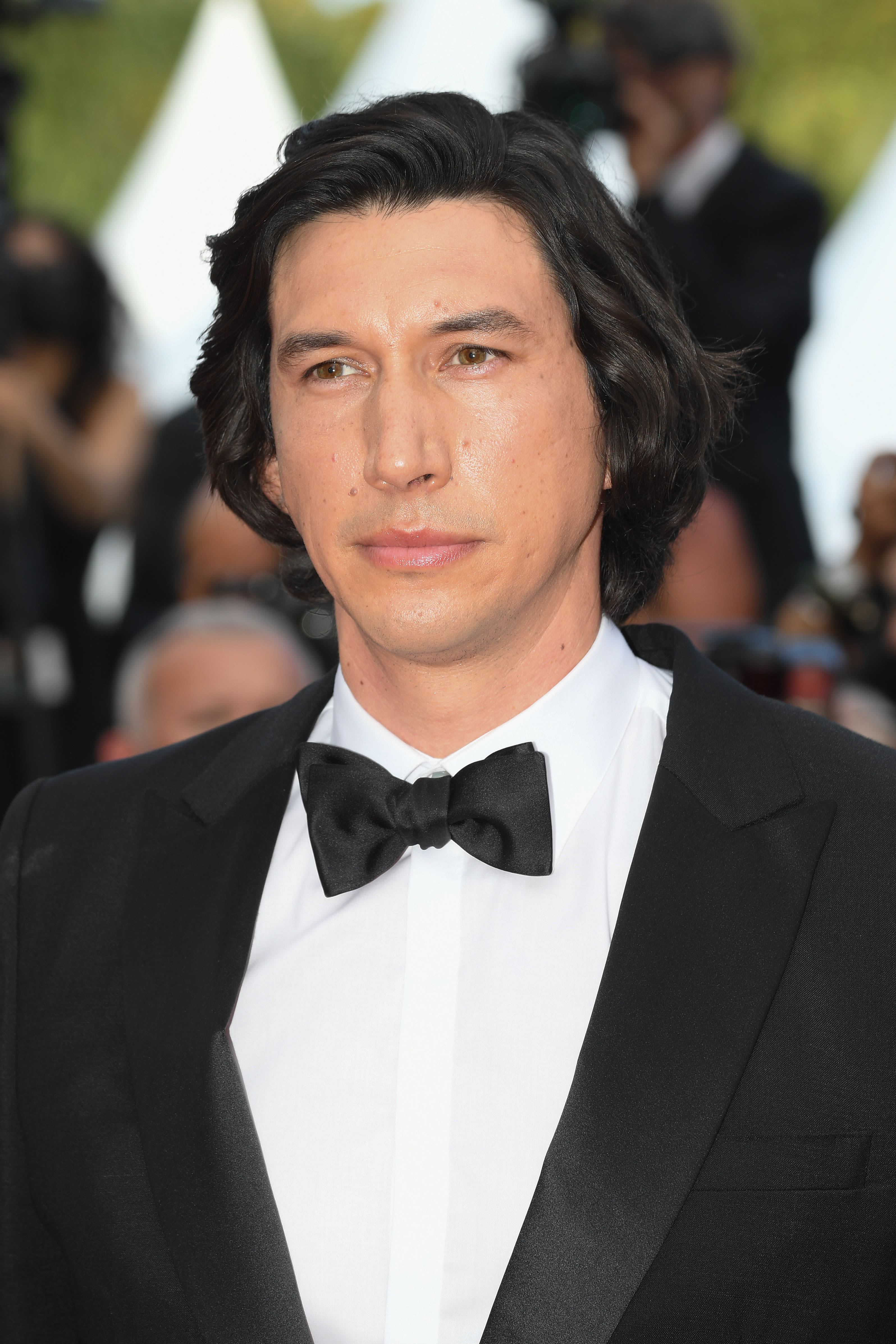 Adam Driver at Cannes Film Festival 2021, wearing a classic black and white tuxedo with a subtle, no-makeup makeup look using Charlotte Tilbury products.