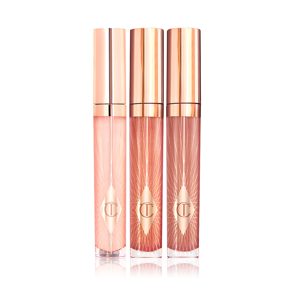Three lip glosses in shades of light pink, coral-peach, and brown-pink in glass tubes with gold-coloured lids. 