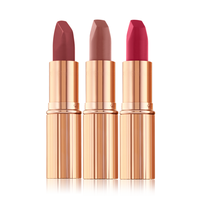 Three open, matte lipsticks in shades of dark red, dark pinkish beige, and magenta in sleek, gold-coloured tubes.