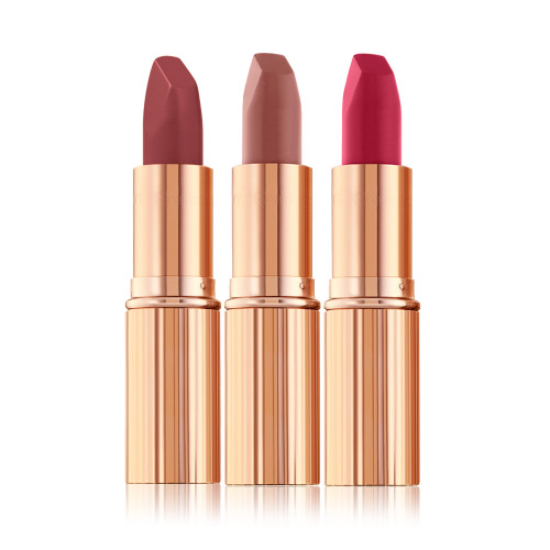 Three open, matte lipsticks in shades of dark red, dark pinkish beige, and magenta in sleek, gold-coloured tubes.