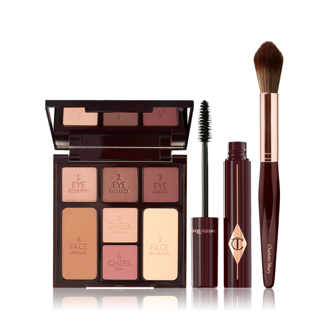 An open, mirrored-lid face palette with nude eyeshadows, blushes, bronzer, and highlighter with an open mascara and blending brush in dark crimson colour.