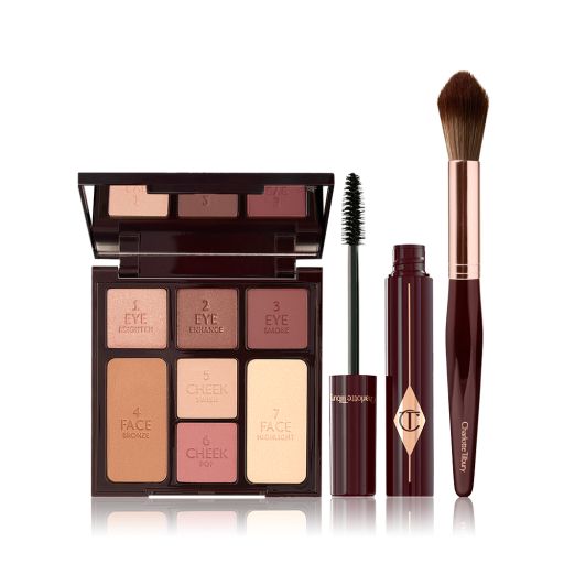 An open, mirrored-lid face palette with nude eyeshadows, blushes, bronzer, and highlighter with an open mascara and blending brush in dark crimson colour.
