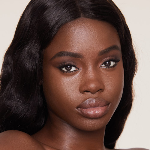 Deep-tone brunette model with flawless, matte skin wearing a nude pink lipstick and black eyeliner.