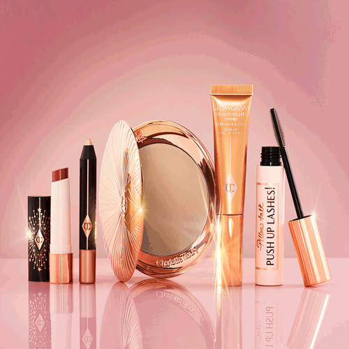 An open lipstick balm, chubby eyeshadow stick in a shimmery champagne colour, bronzer compact, liquid highlighter wand in a soft gold-coloured tube, and a black mascara in a nude pink-coloured tube with a gold-coloured lid.