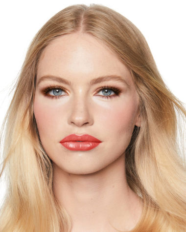 A fair-tone model with blue eyes wearing smokey brown eye makeup with warm bronze and pink blush, and glossy terracotta lips.