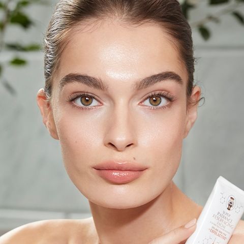 Mannequin à la peau claire, lisse et zéro défaut et aux yeux noisette, tenant un tube blanc d'un masque exfoliant à rincer.